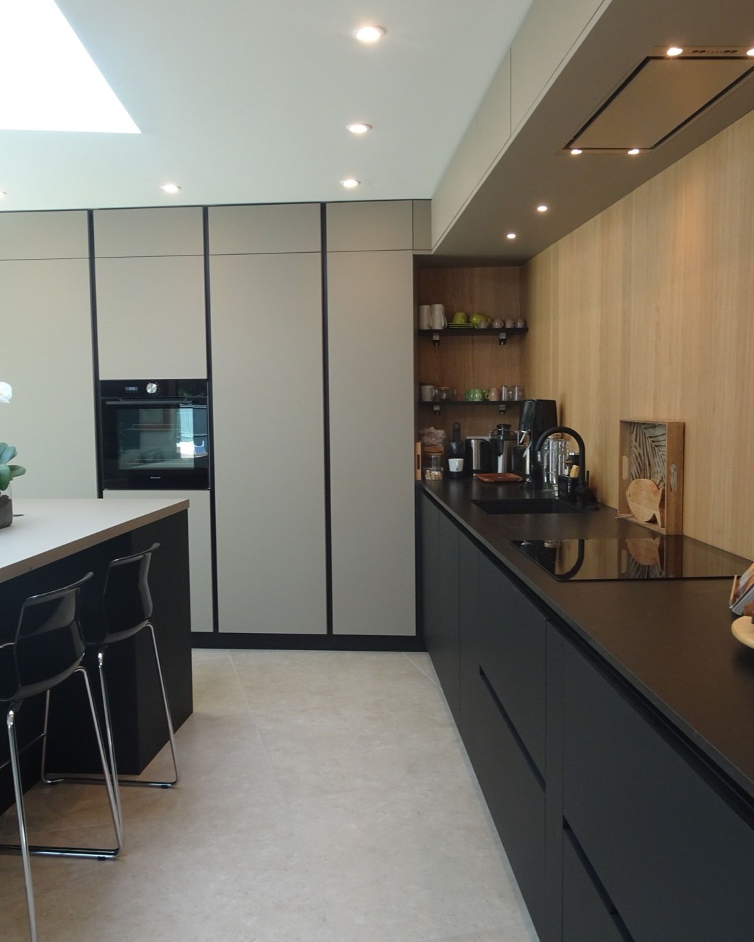 Cuisine contemporaine rénovée en Gironde : îlot central, colonnes de rangement toute hauteur, mur en chêne et plan de travail noir sous verrière de toit