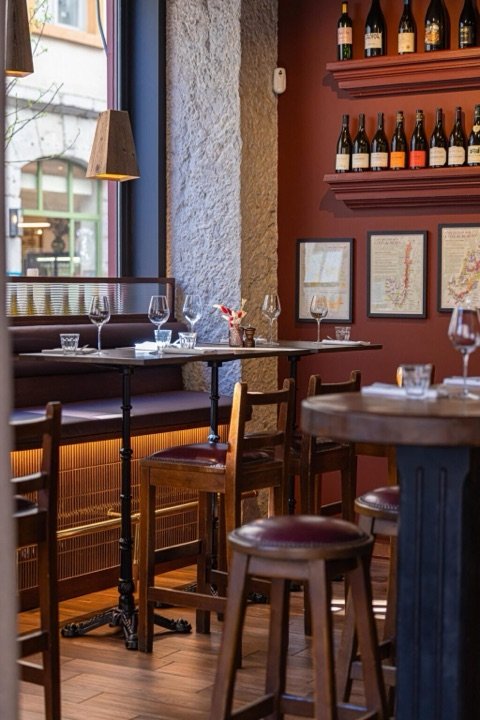 Salle de restaurant rénovée avec mur bordeaux, pierre apparente et banquettes