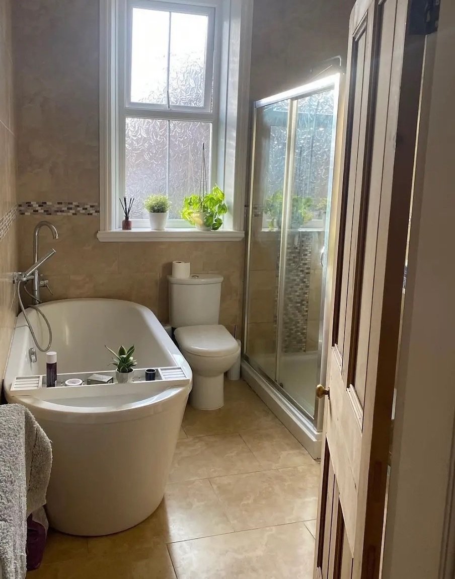 Avant : salle de bains en travertin beige avec baignoire îlot, cabine de douche à portes coulissantes et frise en mosaïque