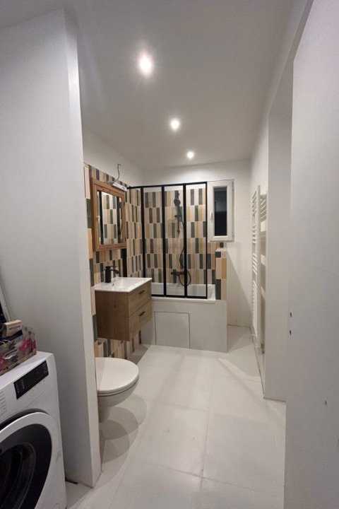 Salle de bains avec baignoire, pare-douche vitré, faïence graphique et coin buanderie